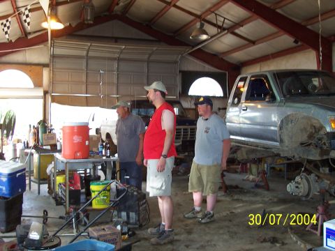 1979 Ford F-150 - A silver pickup truck is undergoing repairs in a cluttered garage, with three men observing.