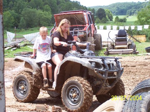 1979 Ford F-150 - A woman and child ride a muddy ATV, with a red off-road vehicle and a riding mower visible in the background.