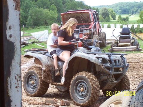 1979 Ford F-150 - A woman and a child ride a muddy ATV, with other vehicles visible in the background.
