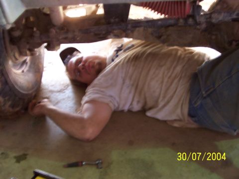 1979 Ford F-150 - A man works on the undercarriage of a vehicle, with a tire visible on the left side.