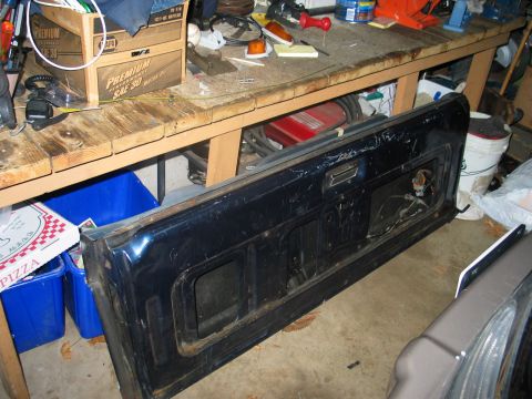 1995 Ford Bronco - A detached vehicle tailgate is shown indoors, resting on the floor near a workbench.