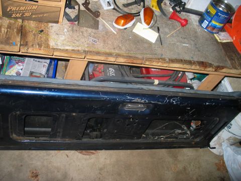 1995 Ford Bronco - A blue tailgate with visible cutouts and a central handle is shown, resting on a workbench.
