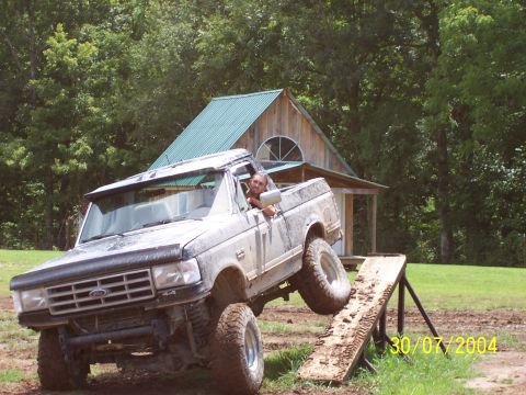 1979 Ford F-150 - A driver maneuvers a lifted Ford F-Series truck over a wooden ramp on an outdoor course.