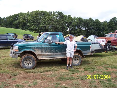 1979 Ford F-150 - A man poses with his muddy green pickup truck at an outdoor event.