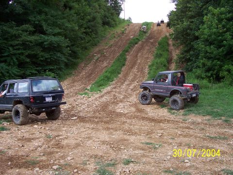 1979 Ford F-150 - Multiple off-road vehicles ascend a steep, rutted dirt incline on a sunny day.