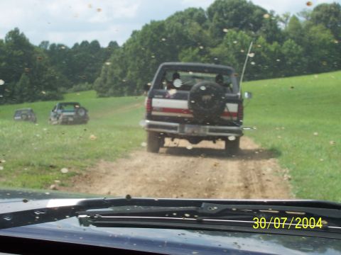 1979 Ford F-150 - A group of vehicles drives down a dirt path through a grassy field on a sunny day.