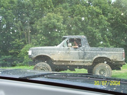 1979 Ford F-150 - Lifted pickup truck covered in mud, seen from another vehicle's dashboard.