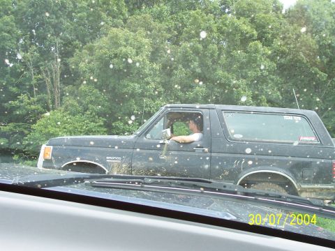 1979 Ford F-150 - A driver navigates a muddy off-road trail in a Ford Bronco, with another vehicle's windshield in the foreground.