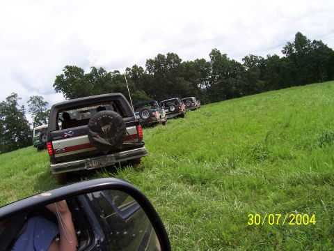1979 Ford F-150 - A line of SUVs, including a black Ford Bronco, navigates a grassy incline on a cloudy day.