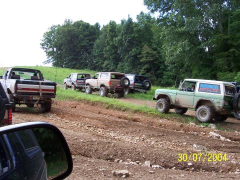 1979 Ford F-150 - Several off-road vehicles, including a green Ford Bronco, are gathered on a dirt track surrounded by trees.