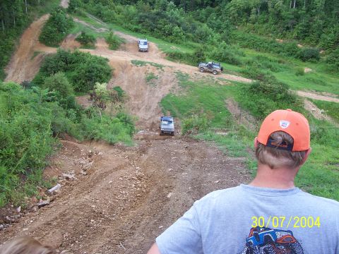 1979 Ford F-150 - Multiple vehicles traverse a challenging off-road course on a sunny day, with a person in the foreground observing the action.