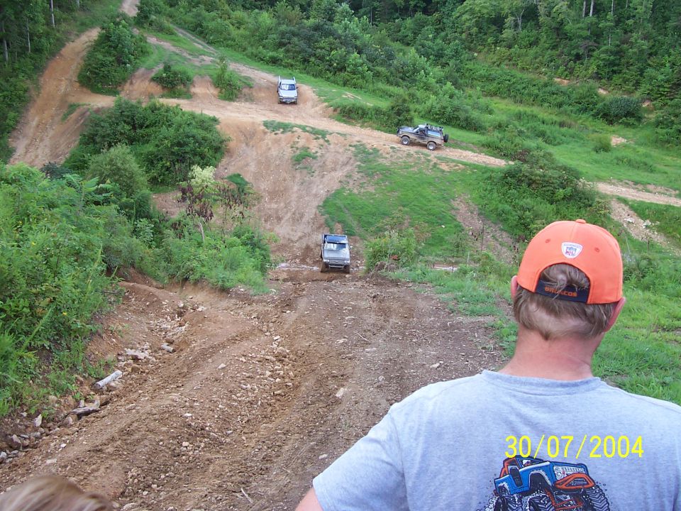 Off-road vehicles navigating a steep dirt track with lush green hills in the background