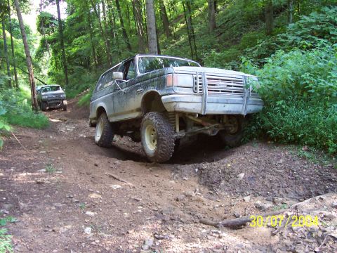 1979 Ford F-150 - Two SUVs navigate a challenging off-road trail through a dense forest.