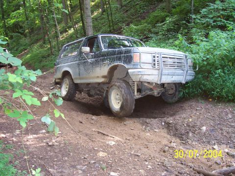 1979 Ford F-150 - A black Ford Bronco navigates a steep, muddy incline on a wooded trail.