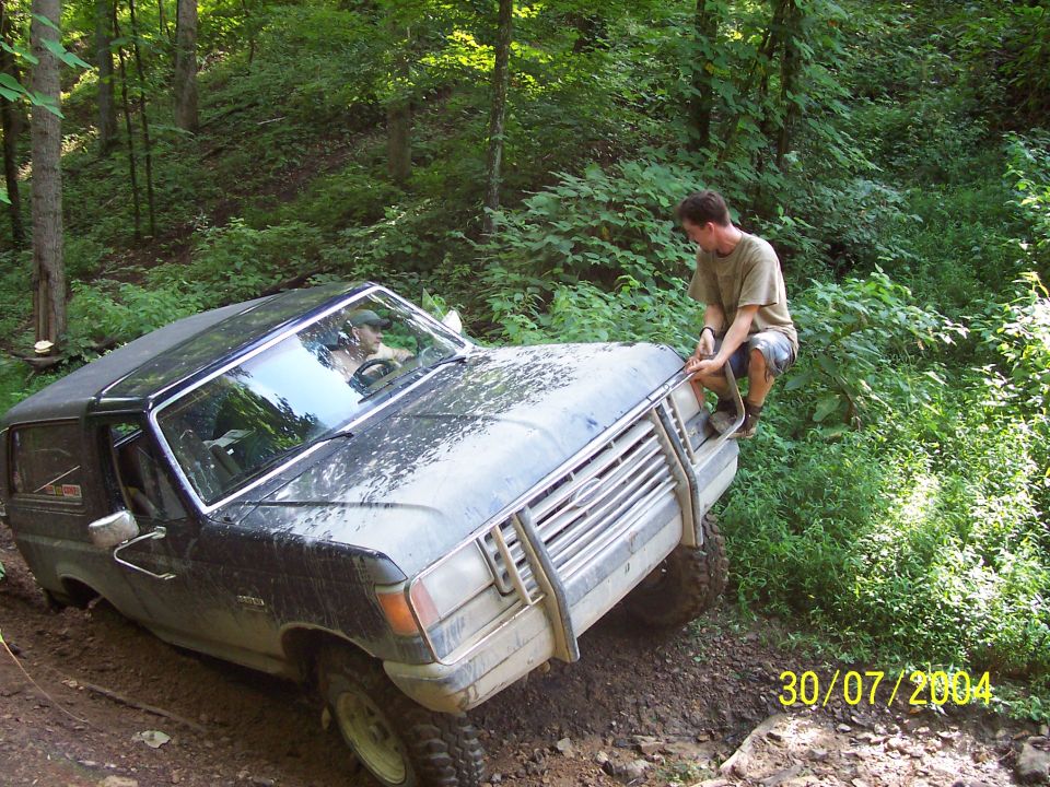Black Ford Bronco with a brush guard stuck in mud on a wooded trail