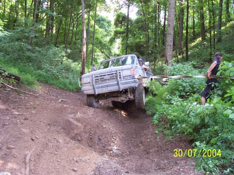 1979 Ford F-150 - A truck navigates a steep, muddy trail in a wooded area, with a person assisting with a tow strap.