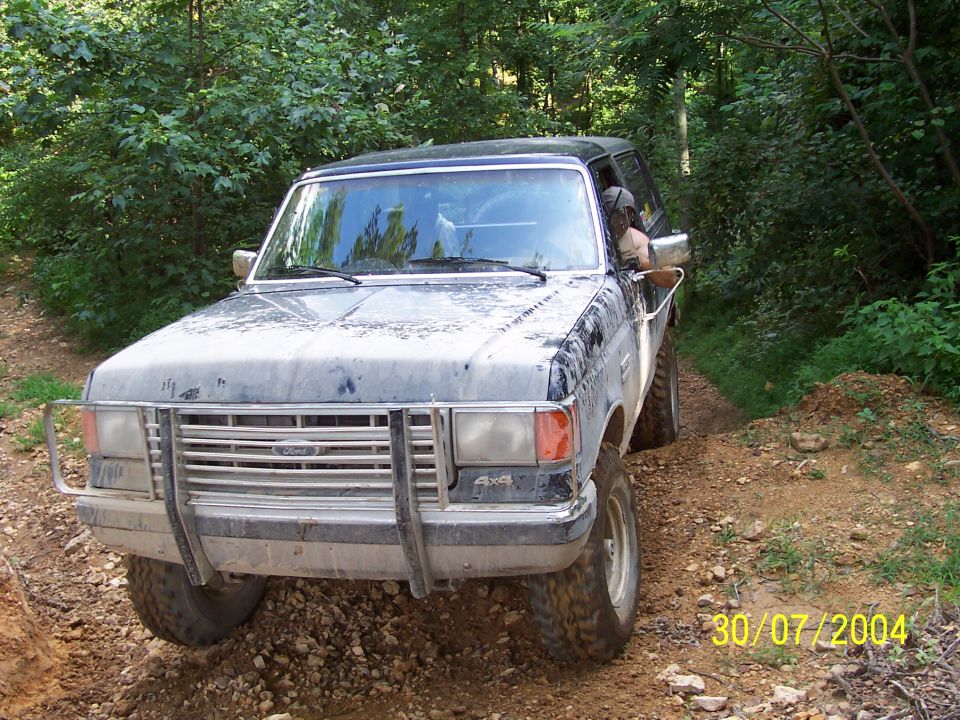 1987 Ford Bronco on a dirt trail, front view. Has a brush guard and 4x4 decal