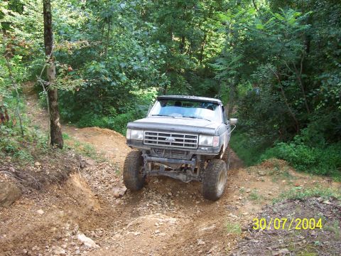 1979 Ford F-150 - A lifted Ford pickup navigates a challenging dirt path surrounded by dense forest foliage.