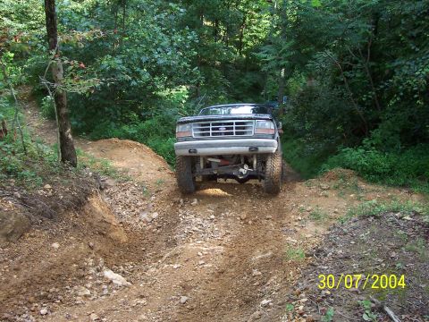 1979 Ford F-150 - A black Ford F-Series truck navigates a challenging dirt path surrounded by dense foliage.