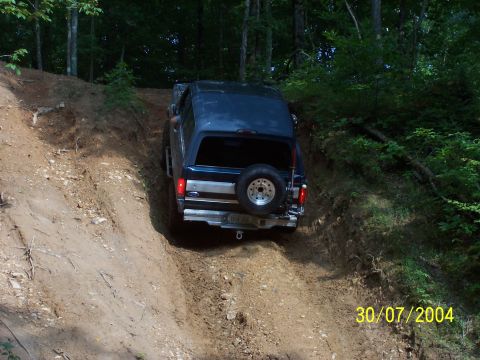 1979 Ford F-150 - A dark blue SUV navigates a steep dirt path in a wooded area.