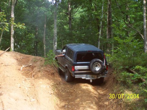 1979 Ford F-150 - A dark blue SUV navigates a steep, wooded dirt trail, kicking up dust as it goes.