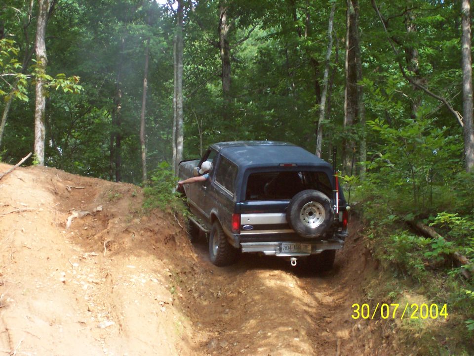 Dark blue SUV with spare tire on rear, driving on a wooded dirt trail