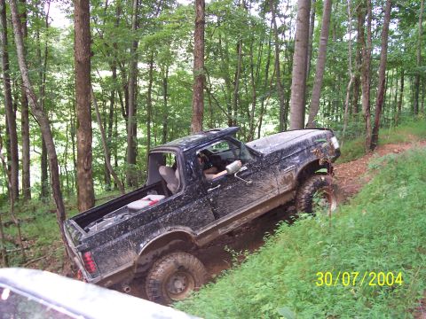1979 Ford F-150 - A black Ford Bronco II navigates a steep, muddy incline in a wooded area.