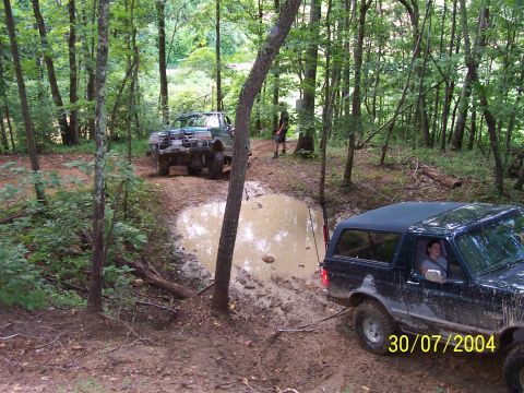 1979 Ford F-150 - Two trucks are seen off-roading through a muddy trail in a forest, with one vehicle partially submerged in a large puddle.