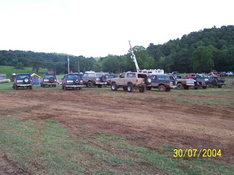 1979 Ford F-150 - A collection of trucks and SUVs are parked in a muddy outdoor area, with trees in the background.