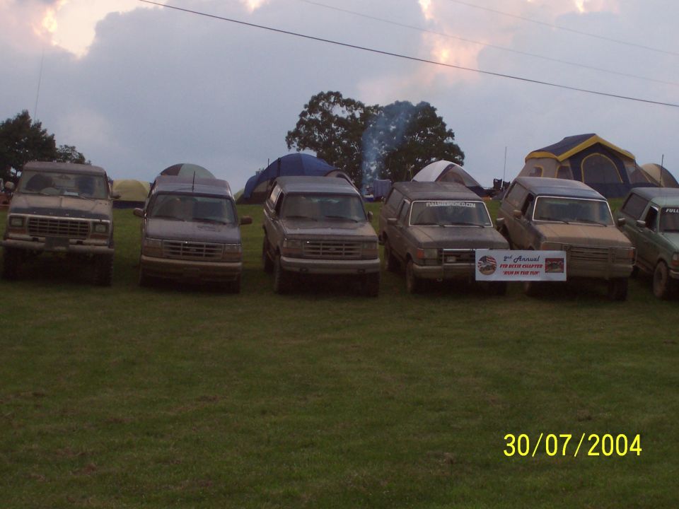 Four vans parked in a grassy field with tents behind them