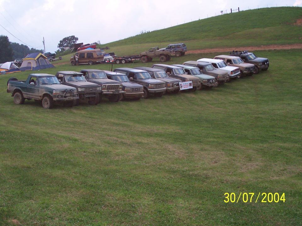 Several trucks and SUVs parked in a grassy field, with tents and a van in the background