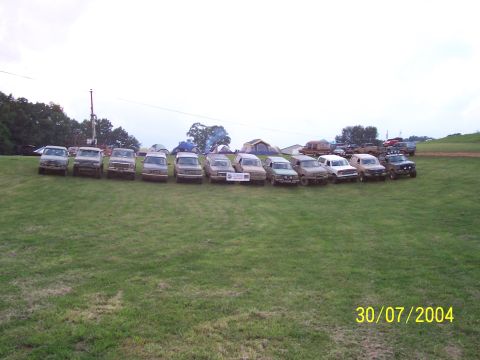 1979 Ford F-150 - Multiple trucks and SUVs are parked in a line on a grassy field with tents in the background.