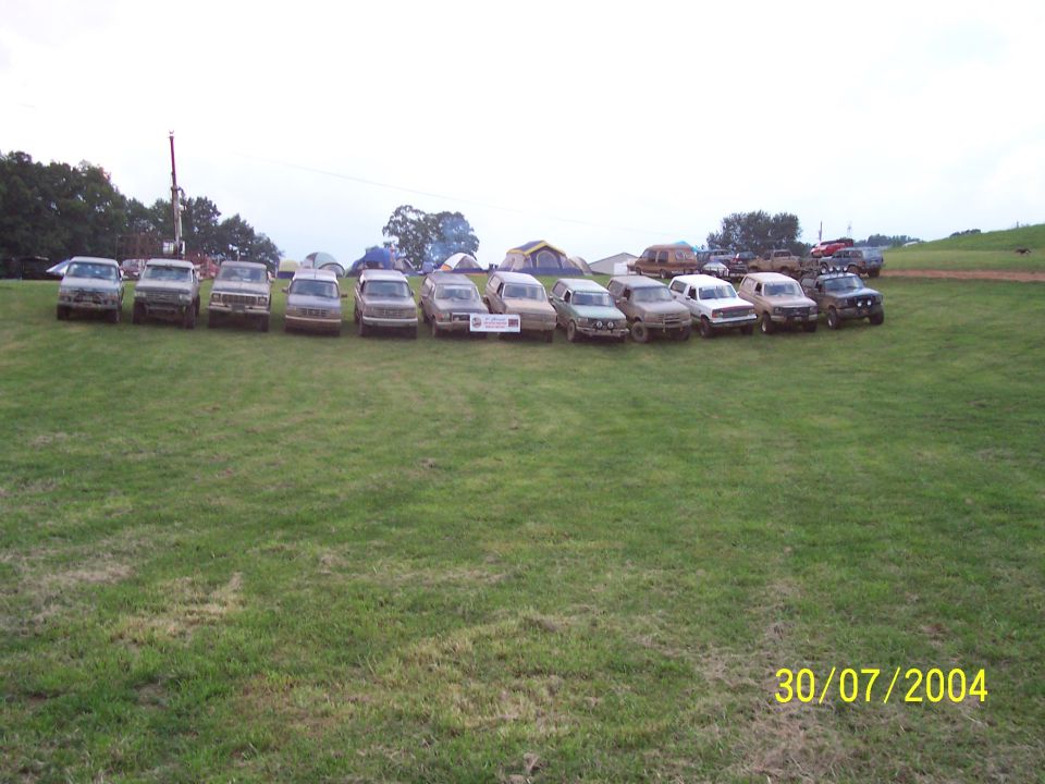Line of trucks and SUVs parked on grass, tents in background. Date stamp 30/07/2004