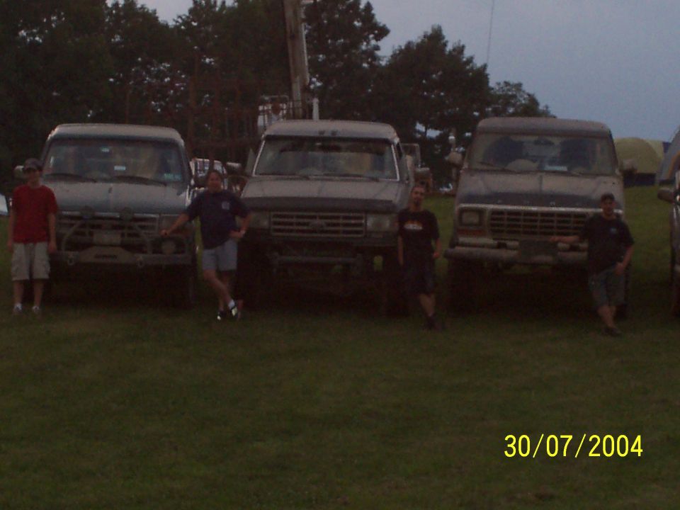 Three trucks parked in a grassy field with two people standing in front of them