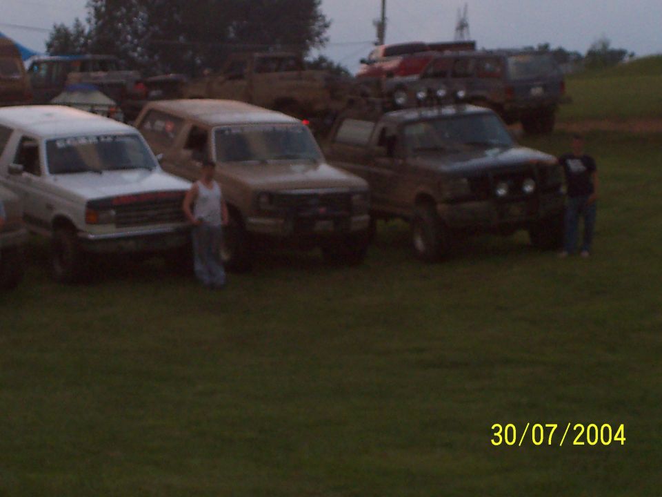 Three trucks and two SUVs parked on grass, with two people standing near them
