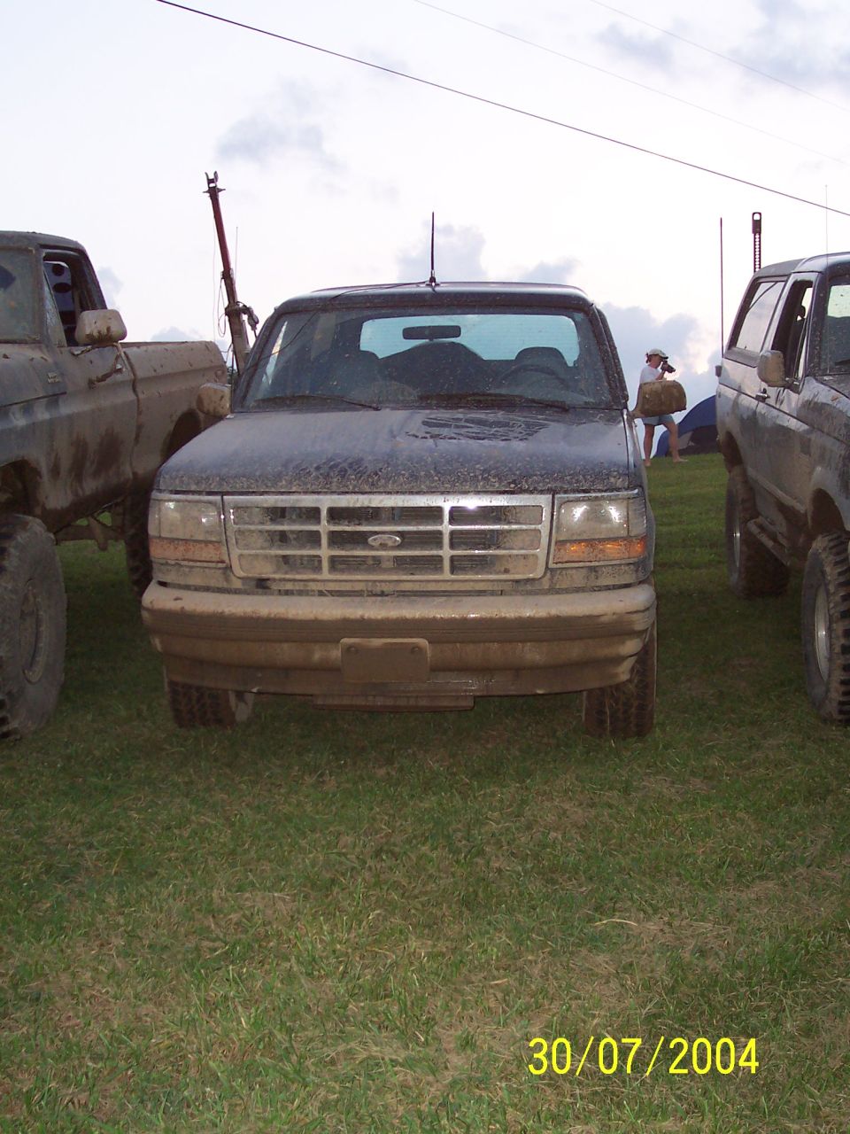 Mud-covered black Ford truck, front view. Grille has horizontal bars and a central Ford emblem. Headlights are rectangular. Tires are large and off-road style