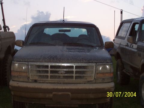 1979 Ford F-150 - Two muddy trucks are parked side-by-side outdoors under a cloudy sky.