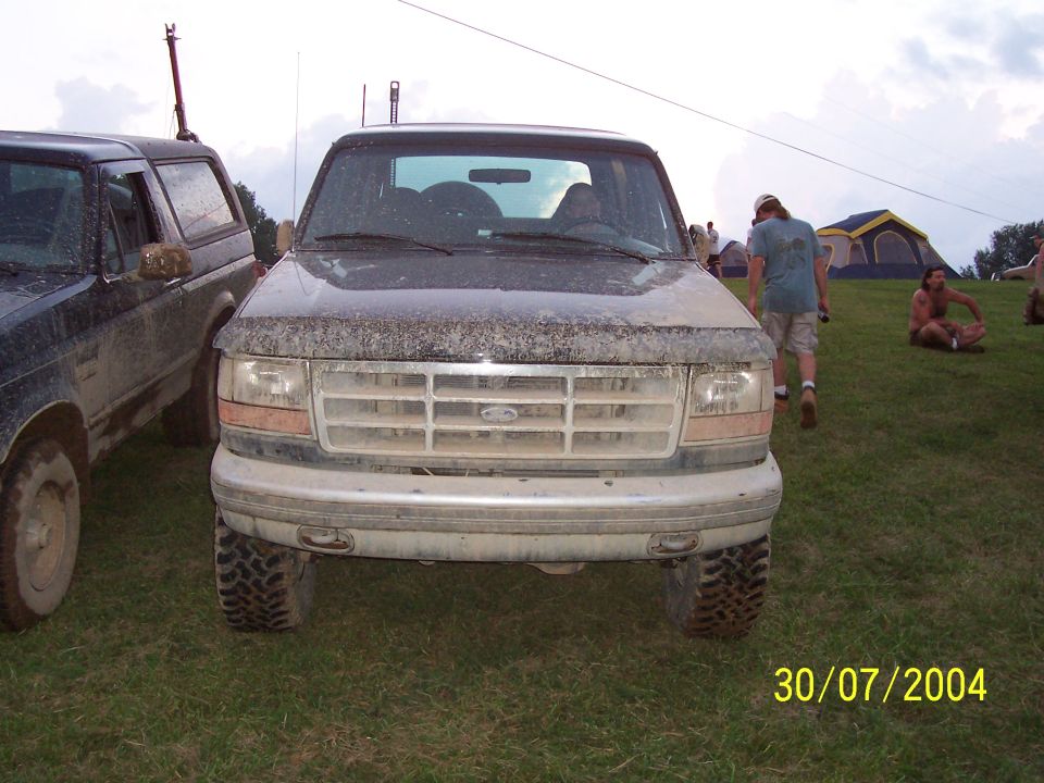 Front view of a dirty Ford truck parked next to another SUV. People and tents are in the background