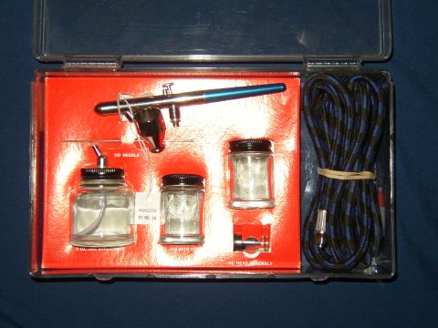 1987 Volkswagen Golf - An airbrush kit is organized in a red insert within a clear plastic case, containing an airbrush, jars, and a hose.