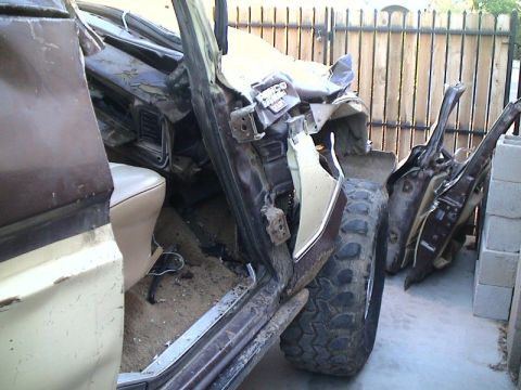 1979 Ford Bronco - A two-tone brown-and-cream truck mid-disassembly in a backyard, viewed through the open door opening with the dash and tan bench seat expos…