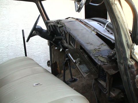 1979 Ford Bronco - Interior of a stripped truck cab shot from the passenger side, showing a badly cracked and peeling brown dash pad, gutted instrument panel…