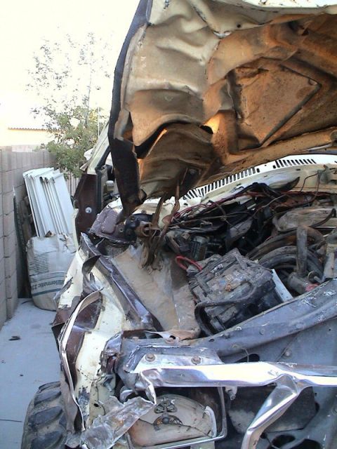 1979 Ford Bronco - Wrecked front end of a white truck with the hood folded up and the underside rusted through, showing crushed fenders, a collapsed core supp…
