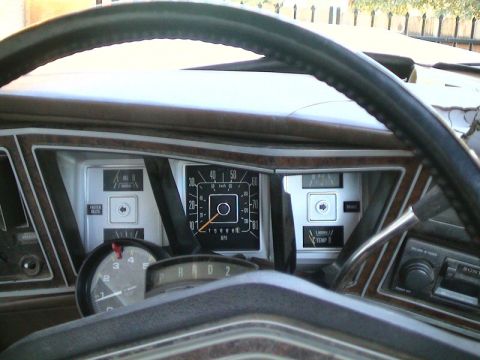 1979 Ford Bronco - View through the two-spoke steering wheel at a woodgrain-trimmed Ford dash: square 10-80 MPH speedometer reading 156,666 miles, flanked by…