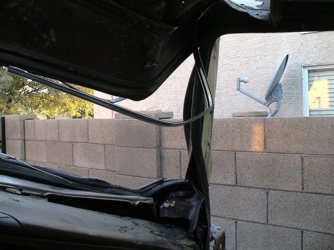 1979 Ford Bronco - A dark vehicle roof and windshield frame partly cut free during a top-removal teardown, with torn sheetmetal, a dangling rubber weatherstri…