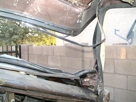 1979 Ford Bronco - Close-up of a stripped brown vehicle body with the roof and windshield frame cut away, exposing rusted, torn sheetmetal, an old weatherstri…