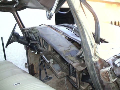 1979 Ford Bronco - Interior of a truck mid-teardown with the windshield glass and roof removed, exposing the bare A-pillars, a weathered brown dash pad with p…