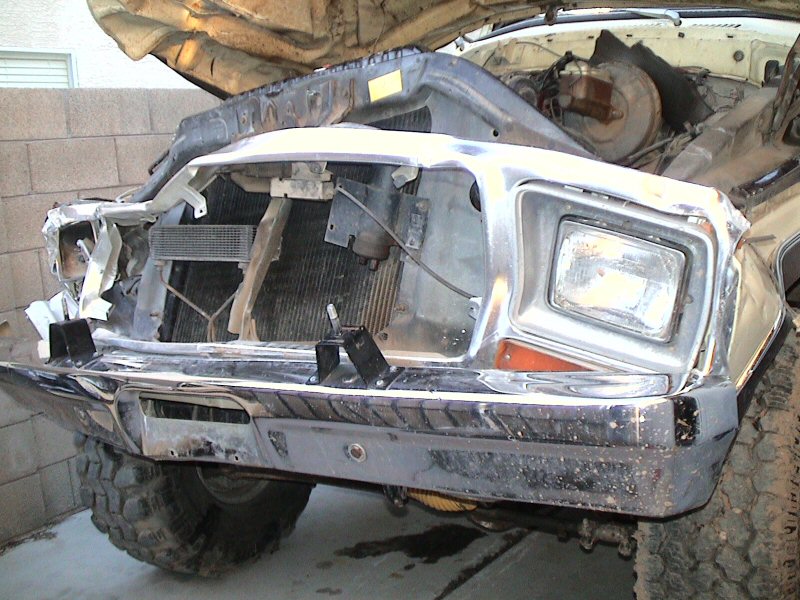 Disassembled front end of a truck with exposed radiator, one headlight, and chrome bumper