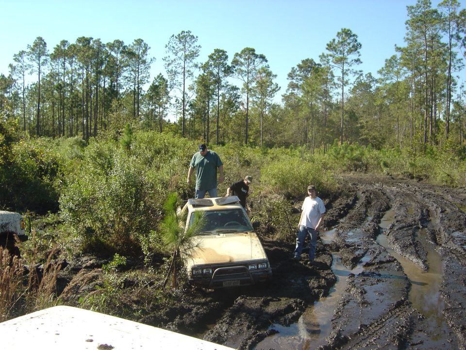 Yellow off-road vehicle stuck in deep mud with three people nearby