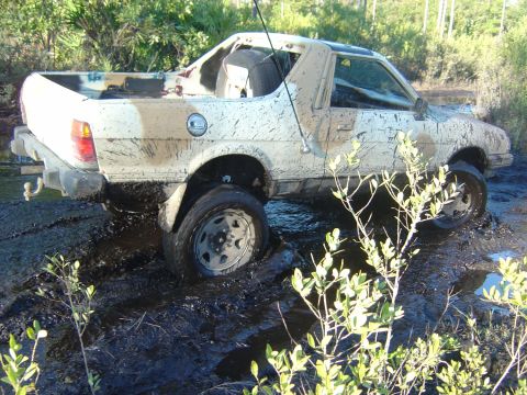 1993 Ford Bronco - A white pickup truck is stuck in thick mud, with its tires submerged.