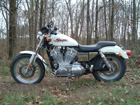 1995 Mercury Grand Marquis - A white Harley-Davidson Sportster motorcycle is parked outdoors in a wooded area.